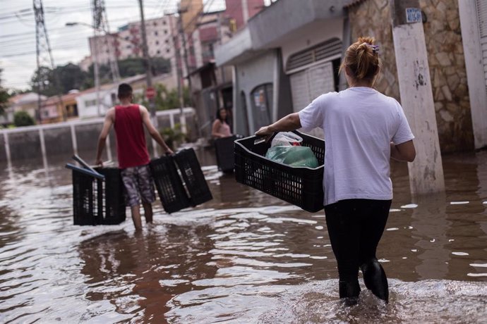 Archivo -  Varias personas vadean una calle inundada tras las inundaciones y corrimientos de tierra provocados por las fuertes lluvias. 