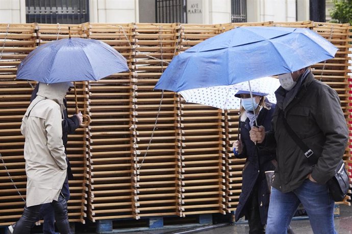 Archivo - Personas pasean con paragüas y mascarilla