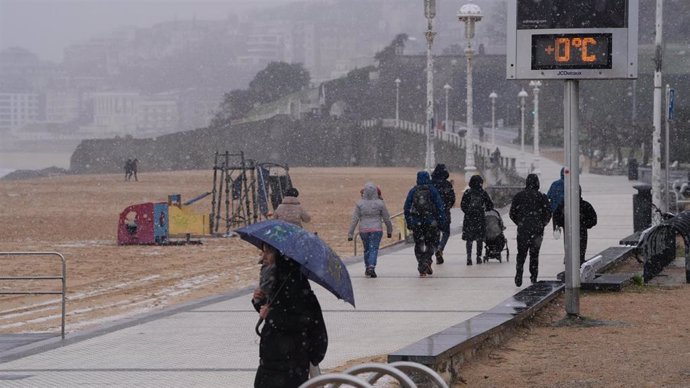 Varias personas pasean por el paseo marítimo de la playa de Ondarreta mientras nieva, a 27 de febrero de 2023, en San Sebastián, Gipuzkoa