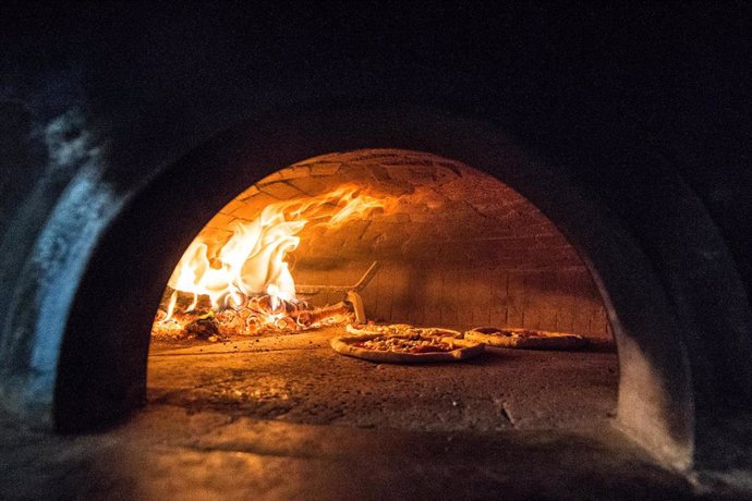 Archivo - Pizzas cocinándose en un horno de leña.
