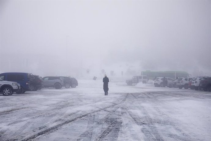 Archivo - Una persona camina por la nieve en el parking del Puerto de Navacerrada