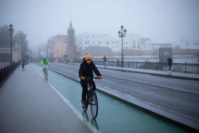 Archivo - Una ciclista se protege del frío con gorro y guantes en el Puente de Triana. A 21 de diciembre de 2022 en Sevilla (Andalucía, España). (Foto de archivo).