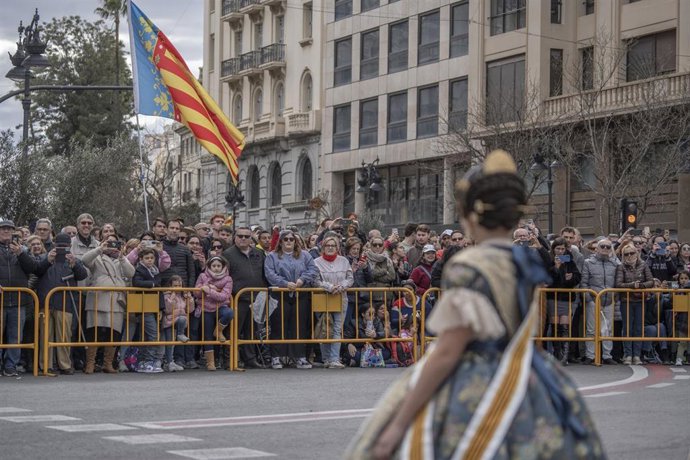 Una fallera camina por delante de las numerosas personas que asisten al encendido de la primera mascletá antes del inicio de las Fallas