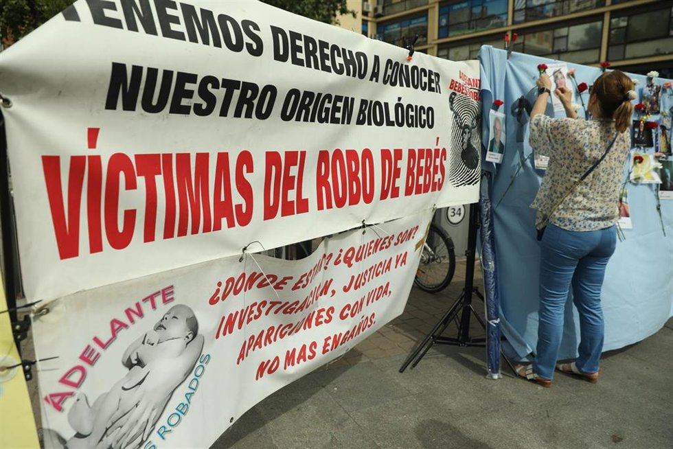 Archivo - Varias personas colocan claveles en un mural colovcado en Madrid con retratos de colaboradores en la búsqueda de víctimas por el robo de bebés en España