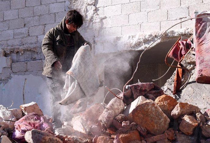 Un niño desplazado recoge sus pertenencias entre los escombros de un edificio destrozado en Alepo (Siria).