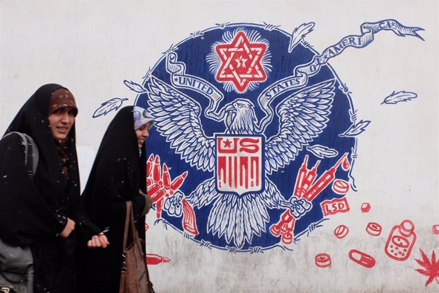 Chicas con velo junto a un mural antiestadounidense en Teherán