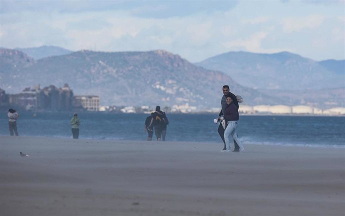 Archivo - Varias personas caminan por la playa mientras les da el viento