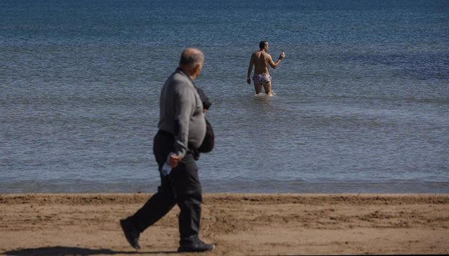 Un hombre pasea mientras uno se baña en la playa de La Malvarrosa, a 10 de marzo de 2023, en Valencia, Comunidad Valenciana (España). 