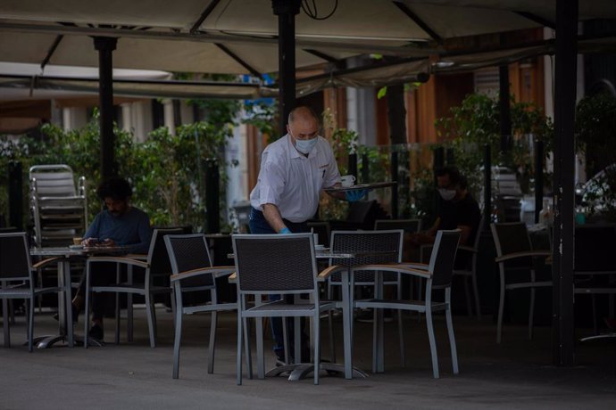 Archivo - Un camarero limpia una de las mesas de la terraza de su bar.