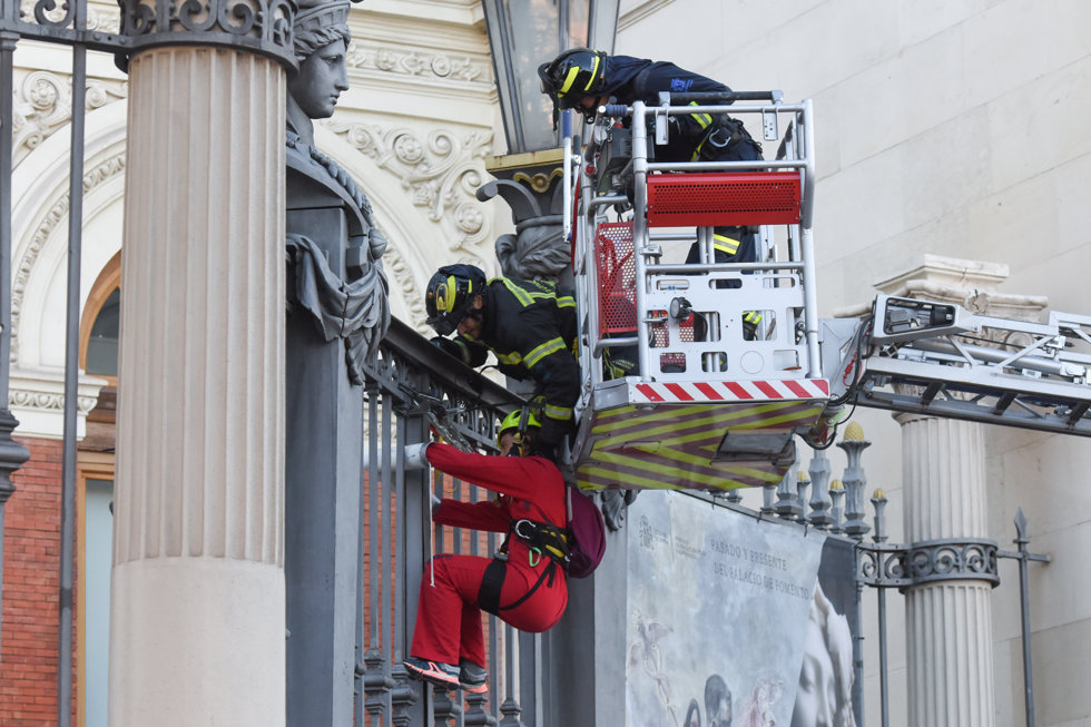 Los bomberos desalojan a una mujer miembro de la organización ecologista Greenpeace, que estaba subida a una de las vallas del edificio del Ministerio de Agricultura, Pesca y Alimentación, a 16 de marzo de 2023.
