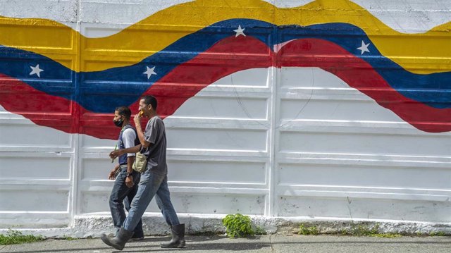 Archivo - Dos personas pasan ante un mural con la bandera de Venezuela en Caracas