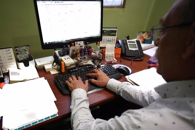Archivo - Un hombre escribe con el teclado de su ordenador, mientras trabaja en el despacho de su oficina.