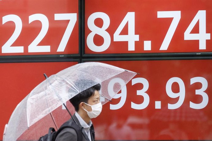 Archivo - 13 July 2020, Japan, Tokyo: A man holds an umbrella as he walks past an electronic stock board showing Japan's Nikkei Stock Average. Photo: Rodrigo Reyes Marin/ZUMA Wire/dpa