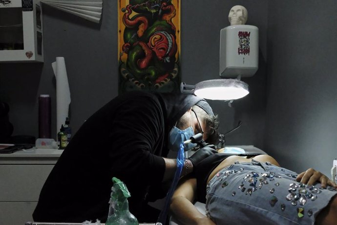 Archivo - Un tatuador realiza un tatuaje a una clienta.