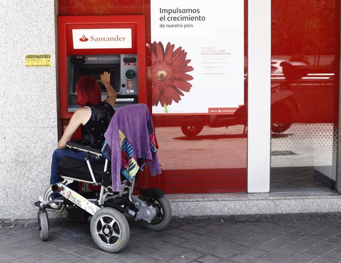 Archivo - Una mujer en silla de ruedas saca dinero en un cajero del Banco Santander en Madrid.