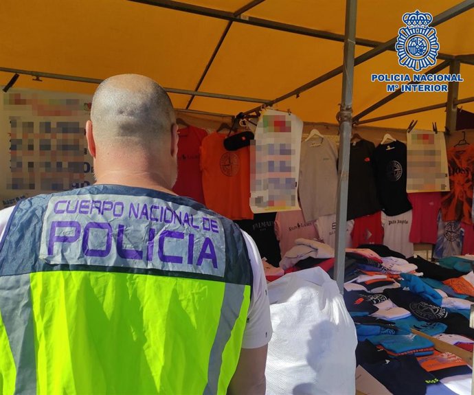 Un agente de la Policía Nacional inspecciona un puesto en un mercadillo en Los Cristianos donde fueron intervenidos más de 1.400 producto de lujo falsificados
