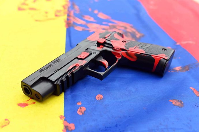 Archivo - Una pistola cubierta de pintura roja sobre la bandera de Colombia