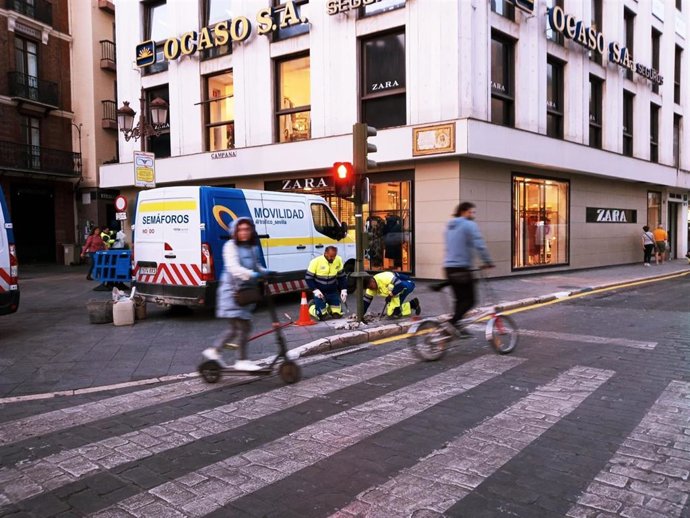 Dos operarios municipales desmontan un semáforo en la Campana por la instalación de las sillas de la carrera oficial de la Semana Santa.