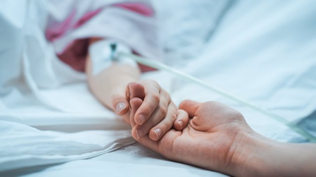 Archivo - Recuperación niño pequeño acostado en la cama del Hospital para dormir, la madre sostiene su mano reconfortante. Se centran en las manos. Emotivo momento familiar.