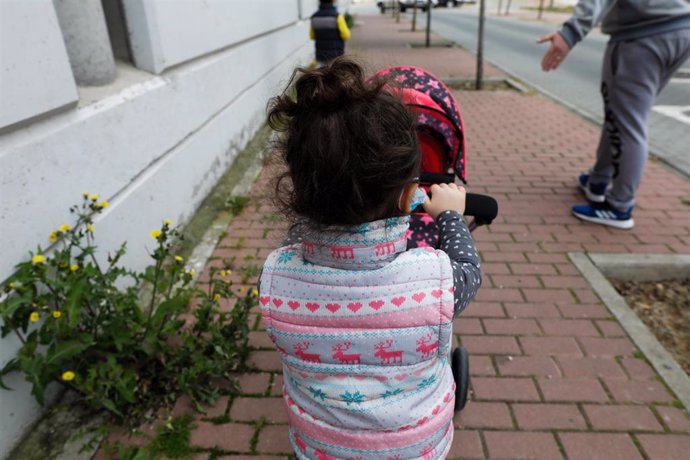 Archivo - Una niña pasea por la calle empujando un carrito con un bebé de juguete 