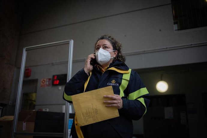 Archivo - Una trabajadora de Correos deja los votos por correo mientras habla por teléfono en una mesa electoral.