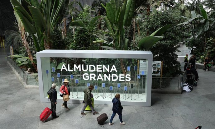 Varias personas caminan frente a la placa de la nueva denominación de la estación Madrid Puerta de Atocha Almudena Grandes como estación Almudena Grandes, en el Jardín Tropical de Atocha-Almudena Grandes.