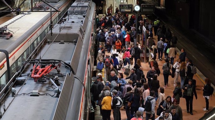 Numerosas personas con maletas esperan en el andén la salida de un tren, en la estación Almudena Grandes-Atocha Cercanías