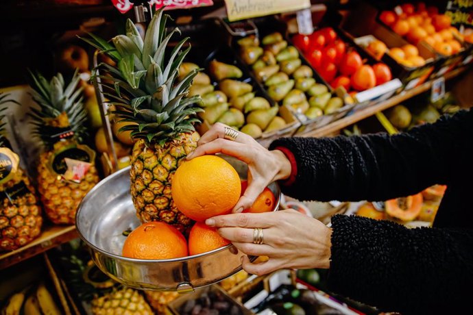 Archivo - Una persona pesa cuatro piezas de naranjas y una piña en la frutería 'Vitaminas', a 2 de enero de 2023, en Madrid (España). El Gobierno ha suprimido durante seis meses el IVA del 4% que se aplica a todos los alimentos de primera necesidad, ent