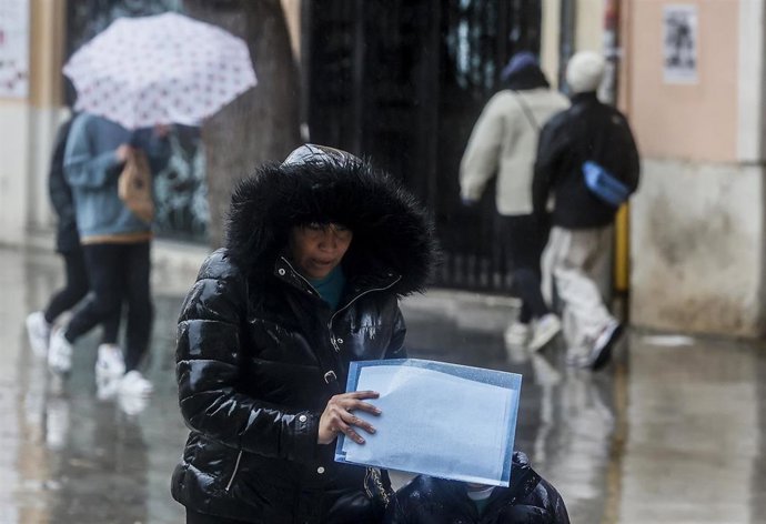 Archivo - Una mujer se tapa la cabeza con la capucha del abrigo como consecuencia de la lluvia en imagen de archivo