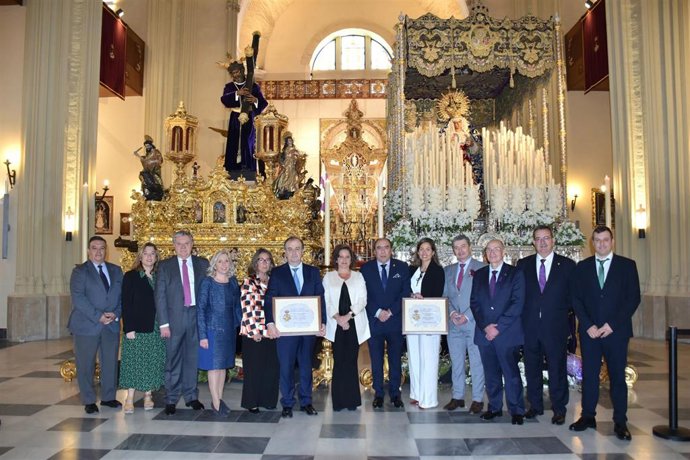 La consejera de Salud y el hermano mayor de Los Gitanos, ambos en el centro de la imagen, posan ante los pasos de la corporación de la Madrugada del Viernes Santo.