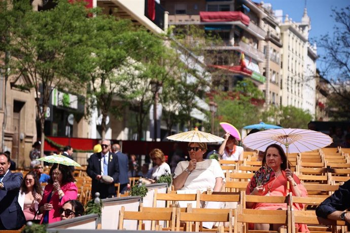 Las personas se protegen del intenso Sol en las sillas de la Campana, esperando la llegada de las cofradías, a 02 de abril del 2023, en Sevilla, (Andalucía, España). 