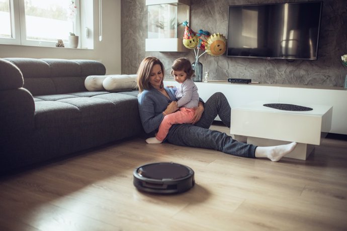 Archivo - One woman, at home relaxing with her little daughter on the floor, while robot vacuum cleaner is working.