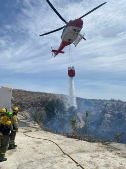 Un helicóptero de la Dirección General de Seguridad Ciudadana y Emergencias descarga agua sobre el incendio