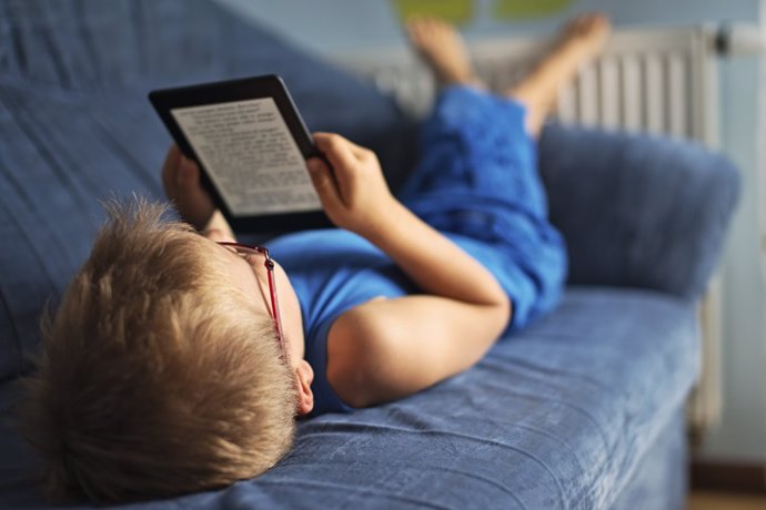 Archivo - Niño con un libro electrónico tumbado en el sofá.