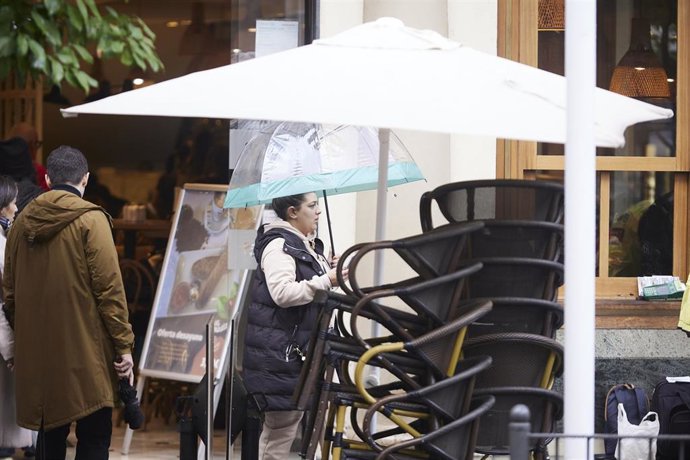 Archivo - Un mujer pasea con su paraguas delante de los veladores de un bar, en una foto de archivo.