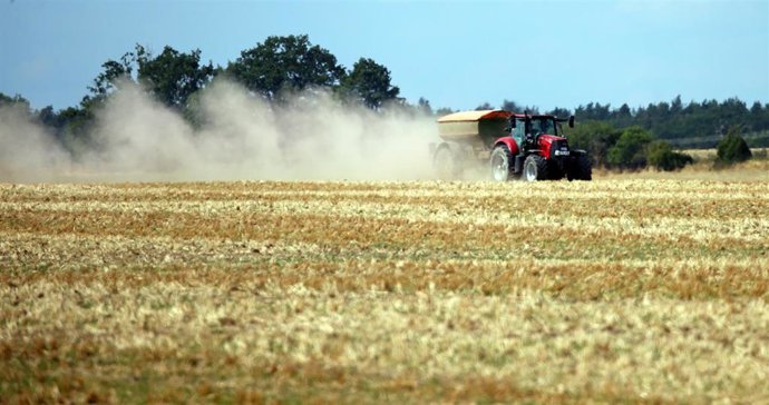 Archivo - 09 August 2022, Berlin: A farmer spreads fertilizer on a harvested grain field near Berlin, dragging a dense cloud of dust behind him. Germany's farmers are warning of the prospect of significant crop failures in the coming months as they stru