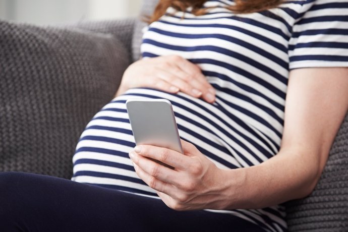 Archivo - Mujer embarazada escribiendo en el móvil