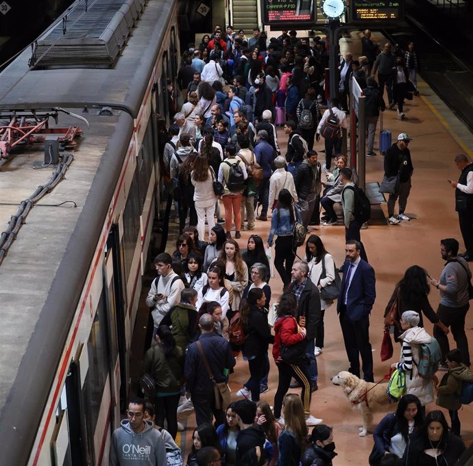 Numerosas personas con maletas esperan en el andén la salida de un tren, en la estación Almudena Grandes-Atocha Cercanías