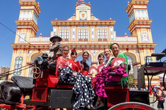 Mujeres vestidas de flamenca con los 'abanicos solidarios', junto a la Portada de la Feria.