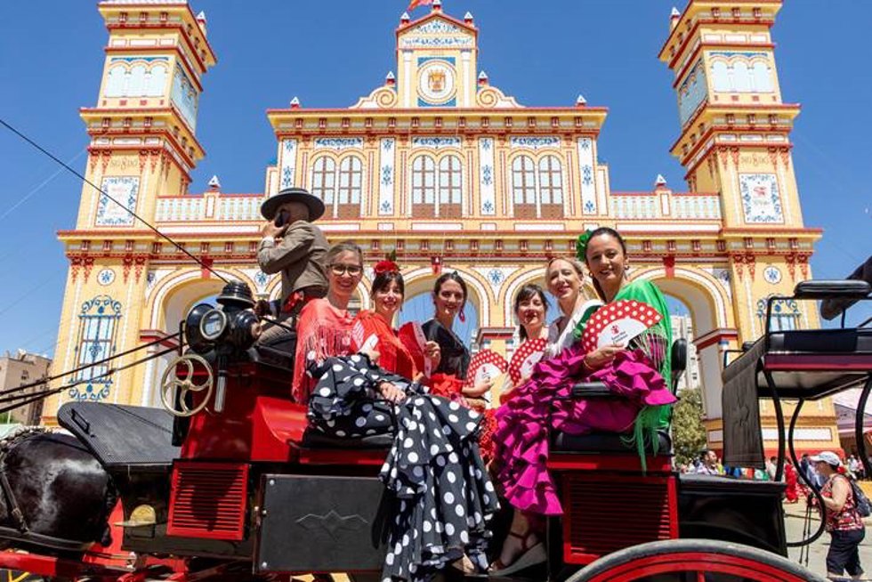 Mujeres vestidas de flamenca con los 'abanicos solidarios', junto a la Portada de la Feria.
