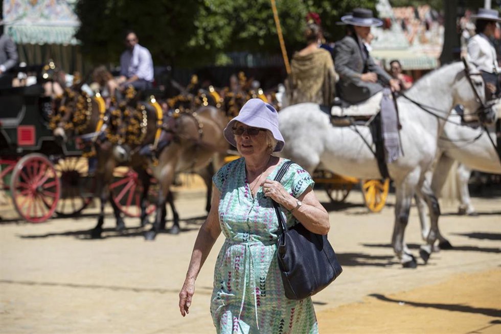 Turistas pasean por el Real de la Feria ataviados con gorros para protegerse del Sol.