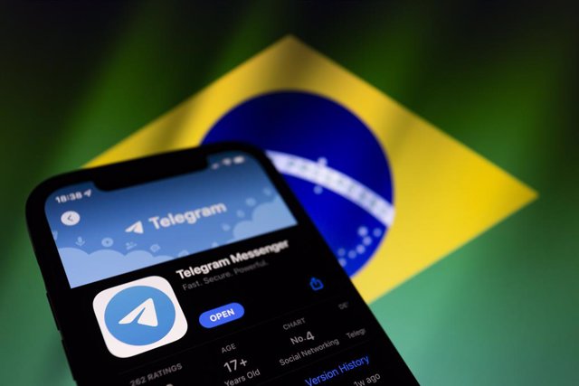 Archivo - March 18, 2022, Asuncion, Paraguay: Illustration: App icon of Telegram on the App Store, on a smartphone backdropped by displayed cropped waving flag of Brazil.