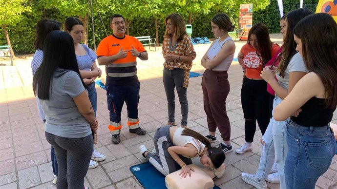 Un profesional sanitario del 061, junto a la delegada de Salud, María Jesús Botella, enseña primeros auxilios a jóvenes estudiantes.