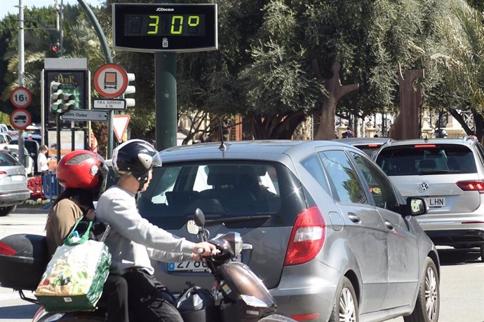 Archivo - Una pareja en moto pasa cerca de un termómetro que marca los 30 grados.