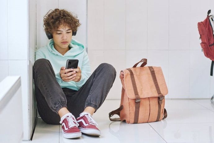 Estudiante sentado en el suelo usando un teléfono móvil