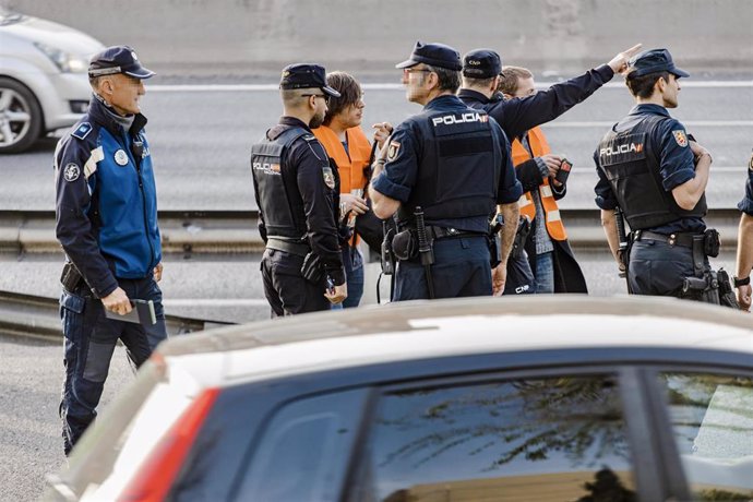 Dos activistas de Futuro Vegetal junto a varios agentes de Policía Nacional tras participar en la acción de colgar dos pancartas en una señal luminosa de la M-30, a la altura de Puente de Vallecas, a 10 de abril de 2023, en Madrid (España). Las dos acti