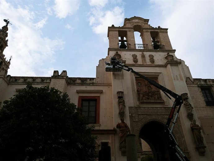 Dos operarios realizan labores de mantenimiento de la Puerta del Perdón desde una grúa.