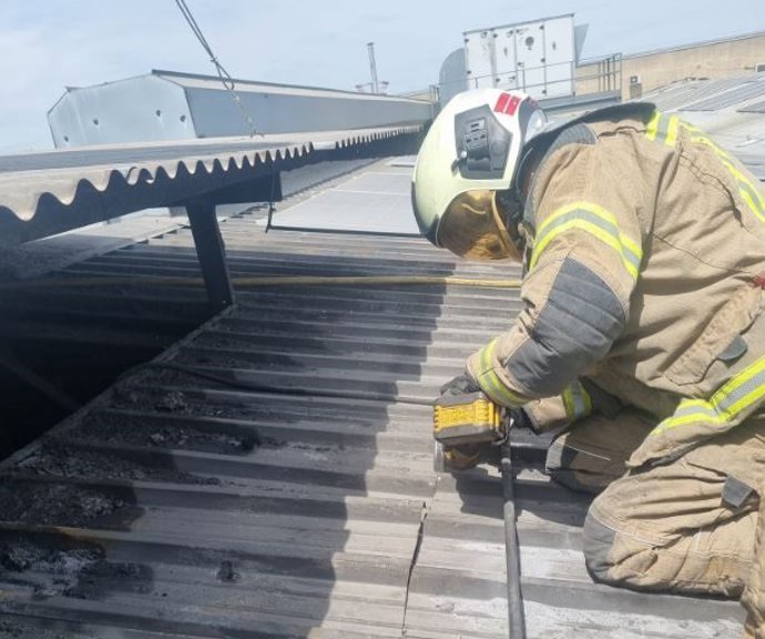 Un bombero trabaja en la cubierta de chapa de la nave en la que se ha producido un incendio en el polígono de San Cristóbal, en Valladolid.