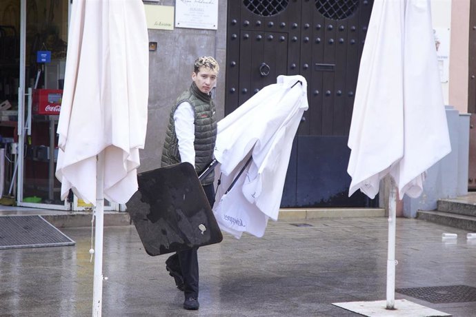 Archivo - Un camarero saca una sombrilla a la terraza de un bar. Imagen de archivo.