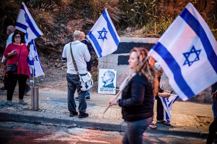 April 22, 2023, Tel Aviv, Israel: Protestors hold the Israeli flag as they walk past a sign showing Israeli Prime Minister Benjamin Netanyahu, during an anti reform demonstration in Tel Aviv. Hundreds of people rallied for the 16th straight week Saturda